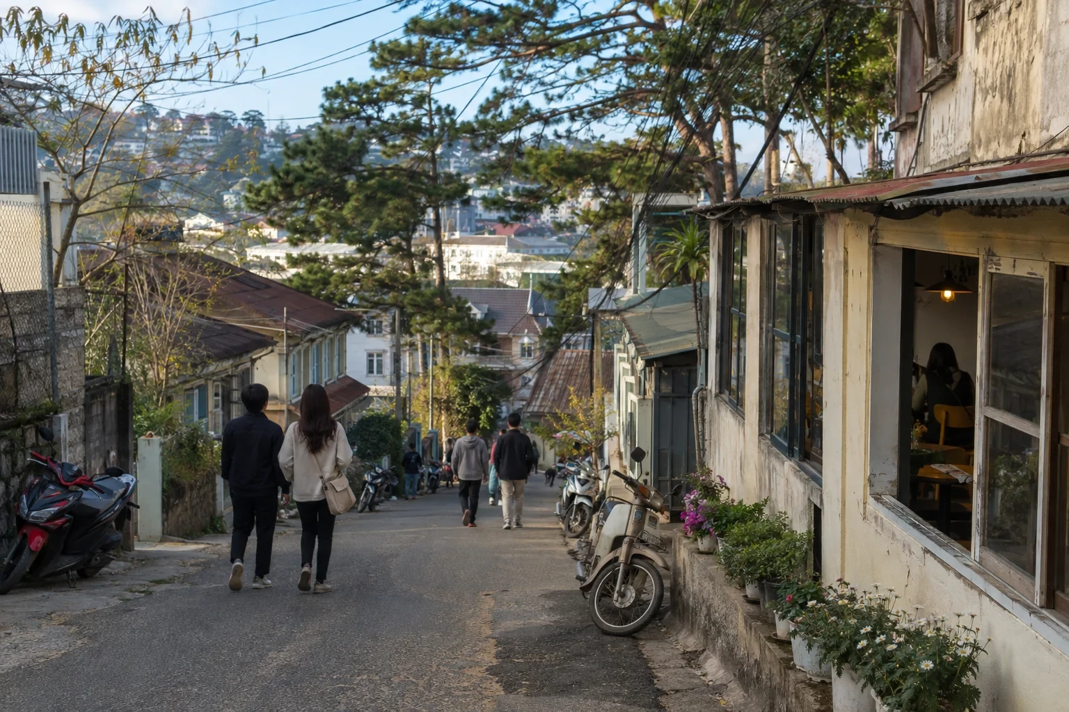 Người trẻ đi trên phố dốc có quán nhỏ, nhà cũ, xe máy và hàng thông