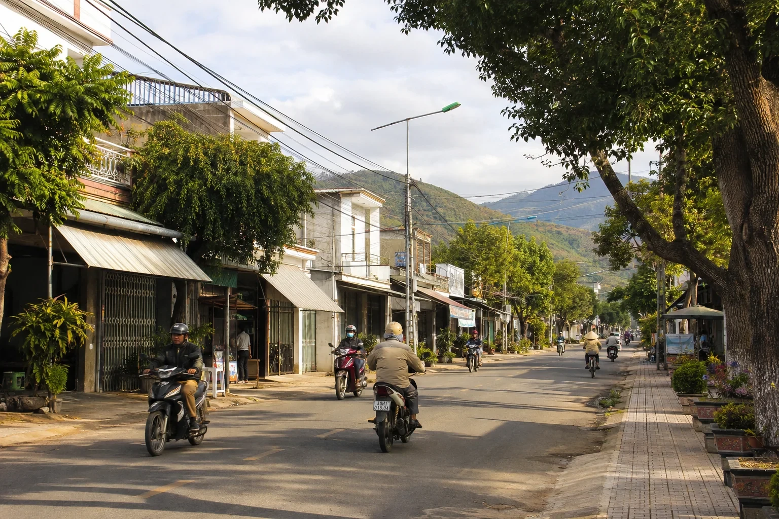 Phố cao nguyên với nhà thấp, hàng cây và xe máy đi lại tự nhiên